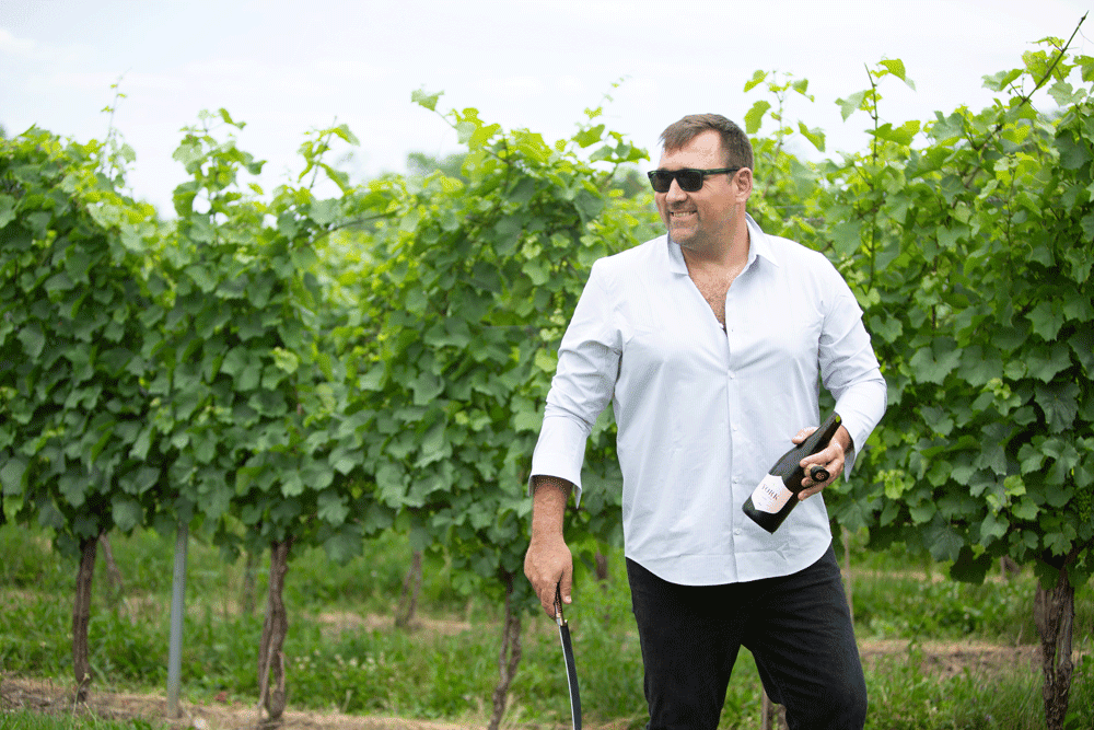 Marty Werner holding a bottle of sparkling wine and a sabre in a vineyard